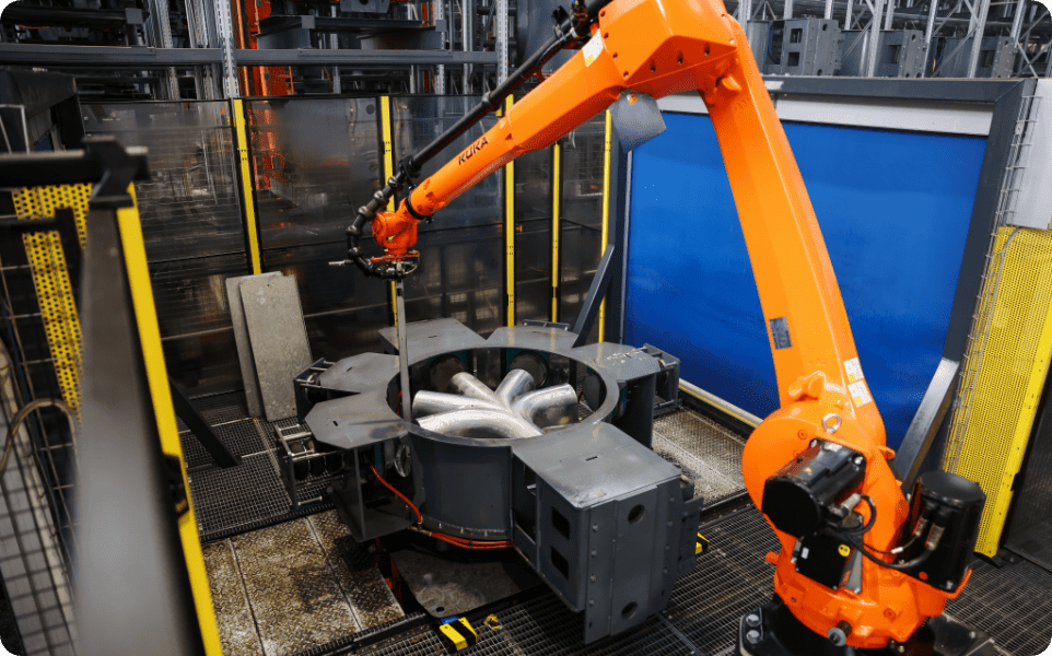 Bras robotisé industriel orange manipulant un composant métallique dans une usine